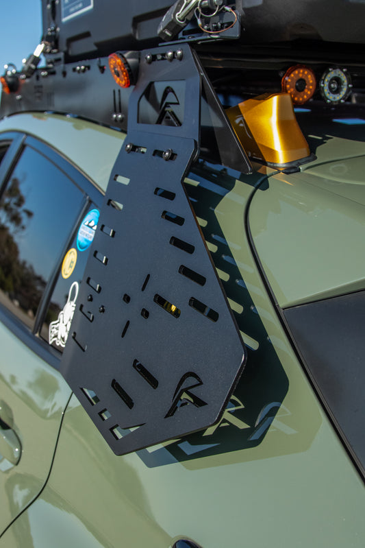 A black metal roof rack with wing mounted onto the rear of an olive green Subaru